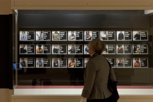A visitor in the Object Stories gallery encounters the large display depicting community members who have recorded stories about personal objects.